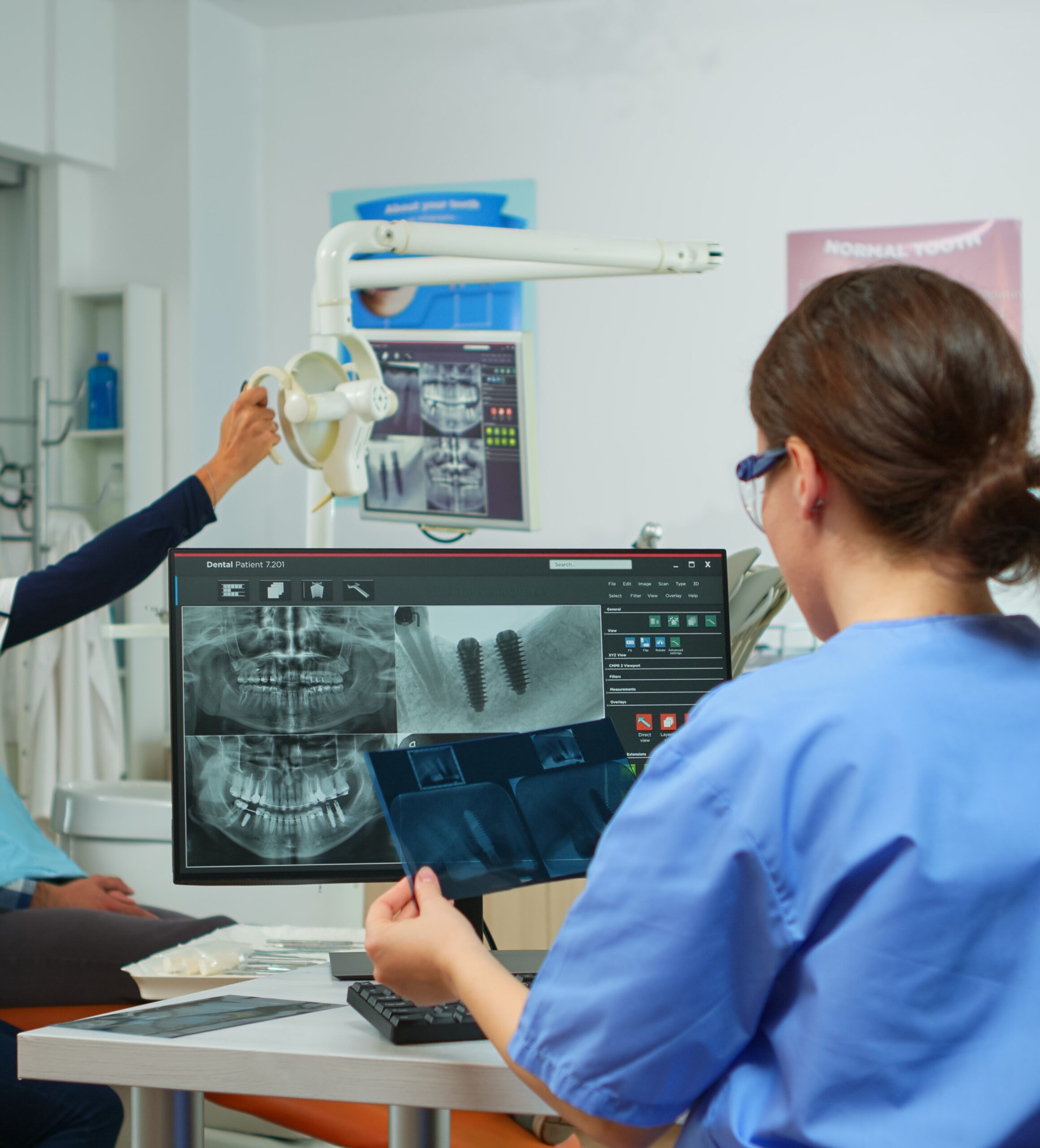 Stomatologist nurse comparing radiographics looking at computer, while specialist doctor with face mask speaks to man with toothache sitting on stomatological chair preparing tools for surgery